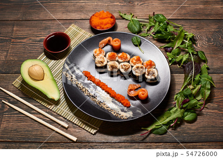 Top view of appetizing Japanese sushi rolls in big black plate, serving with fish slices, sauces Top view of appetizing Japanese sushi rolls in big black plate, serving with fish slices, sauces 54726000