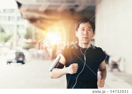 Young Asian man running in the city and wearing headphone Young Asian man running in the city and wearing headphone 54732031