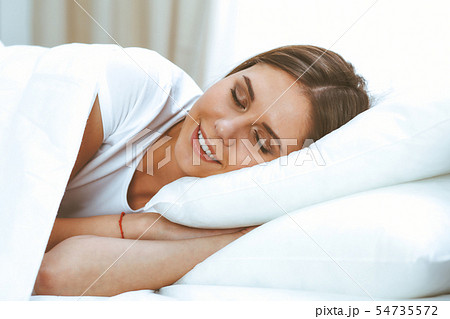 Beautiful young and happy woman sleeping while lying in bed comfortably and blissfully smiling Beautiful young and happy woman sleeping while lying in bed comfortably and blissfully smiling 54735572