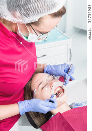Close-up of a dentist applying polymer from a syringe to the inside of a young patient's front tooth Close-up of a dentist applying polymer from a syringe to the inside of a young patient's front tooth 54754988