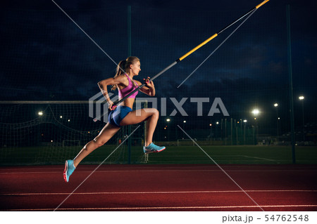 Female pole vaulter training at the stadium in the evening Female pole vaulter training at the stadium in the evening 54762548