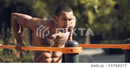 Muscular Guy Doing Street Workout, Exercising On Parallel Bars 54768377