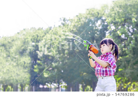 新緑の樹木を背景に水鉄砲で遊ぶ幼い女の子 遊び 幼児 夏休み 楽しみ 自由イメージの写真素材