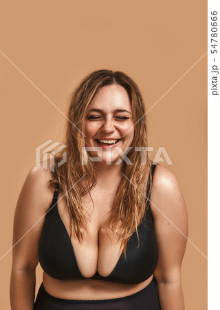 Carefree and happy. Positive plus size woman in black underwear laughing while standing against Carefree and happy. Positive plus size woman in black underwear laughing while standing against 54780666