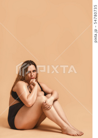 Feeling sad. Vertical photo of plus size sexy model in black lingerie sitting on the floor and 54780735