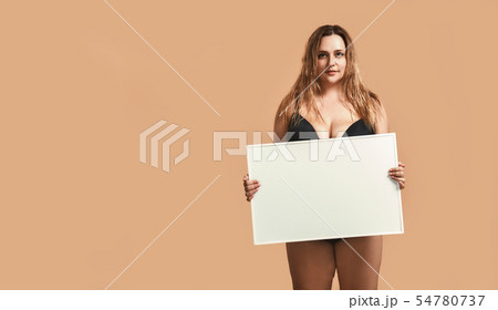 Your text here. Pretty and confident plus size young woman in black lingerie holding empty blank 54780737
