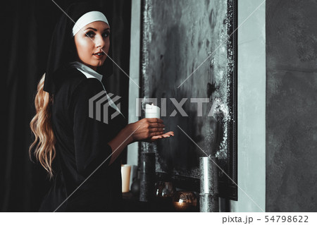 Young catholic nun is holding candle in her hands. Photo on black background 54798622