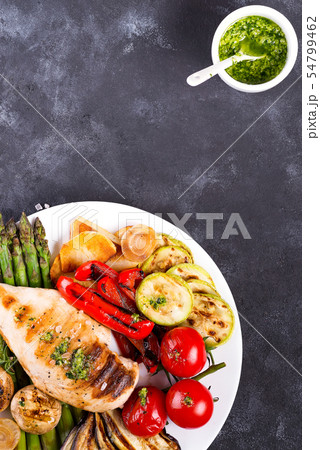 Chicken breast grill with bbq vegetables and pesto sauce in a plate on a concrete background, flat Chicken breast grill with bbq vegetables and pesto sauce in a plate on a concrete background, flat 54799462