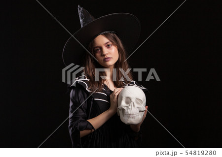 Beautiful child dressedup in a black dress for halloween carnival with a human skull in hands Beautiful child dressedup in a black dress for halloween carnival with a human skull in hands 54819280