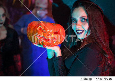 Close up portrait of beautiful woman dressed up like a witch for halloween holding a pumpkin 54819530