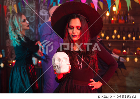 Thoughtful young woman in halloween costume looking at her human skull 54819532
