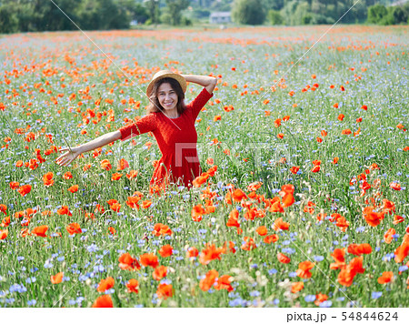 Lovely young romantic woman in straw hat on poppy flower field posing on background summer. Wearing 54844624