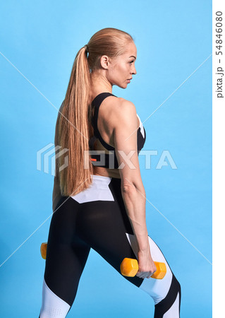 Strong woman with ponytail working out with dumbbells, flexing her arm. 54846080