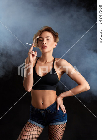 arrogant blonde model in top , shorts, fishnet holding a cigarette 54847568