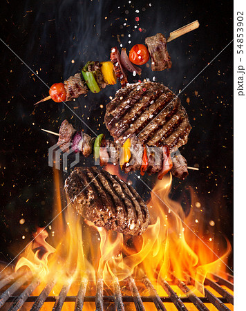Tasty beef steaks and skewers flying above cast iron grate with fire flames. 54853902