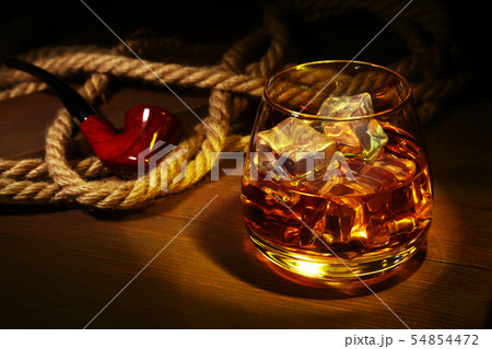 Glass with whiskey, ice cubes and smoking pipe on wooden background. 54854472
