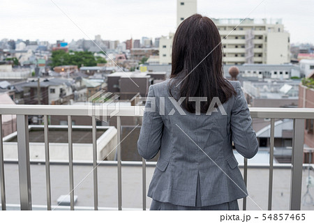 屋上でフェンスに寄りかかる女性の後ろ姿の写真素材
