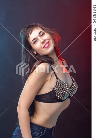 Attractive young sexy brunette woman in riveted top posing in the studio on a dark background Attractive young sexy brunette woman in riveted top posing in the studio on a dark background 54861841