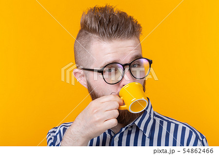 Cute confident young man drinking coffee from a little yellow mug while standing against a yellow 54862466