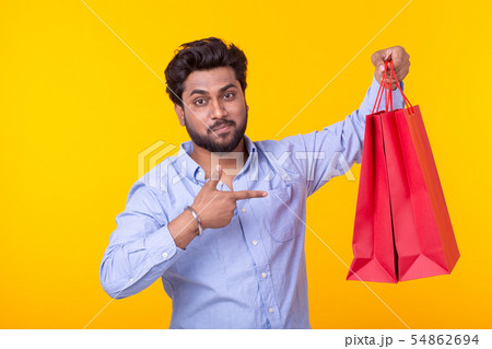 Joyful indian man is holding red shopping bags on a yellow background. The concept of shopping in 54862694