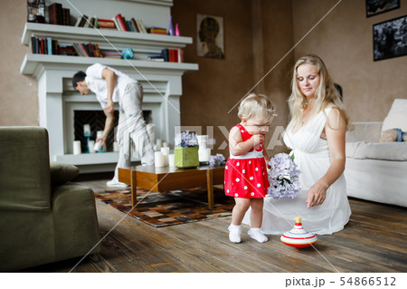 Pregnant woman in white dress playing with one year old baby sitting on a floor 54866512