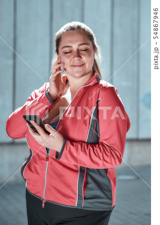 Enjoying workout. Happy plus size woman in headphones holding smart phone and listening music with Enjoying workout. Happy plus size woman in headphones holding smart phone and listening music with 54867946