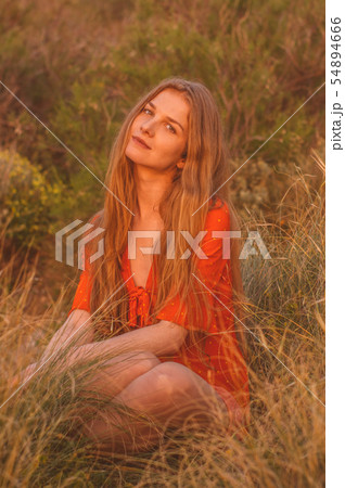 Young blonde girl in red dress sitting on grass Young blonde girl in red dress sitting on grass 54894666