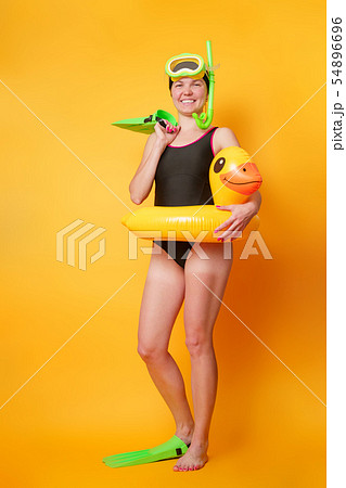 Photo of woman in black bathing suit in flippers with rubber ring in shape of duckling on orange 54896696