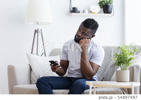 Young man watching tv, using remote control to switch channels 54897497