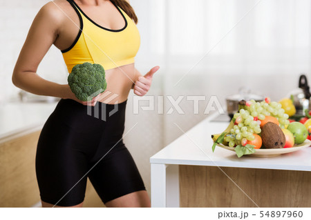 Weight loss concept. Girl holding broccoli and showing thumb up Weight loss concept. Girl holding broccoli and showing thumb up 54897960