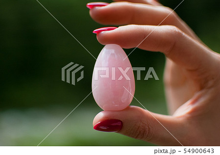Close up photo of female hand holding a yoni egg. Rose quartz crystal egg on river background Close up photo of female hand holding a yoni egg. Rose quartz crystal egg on river background 54900643