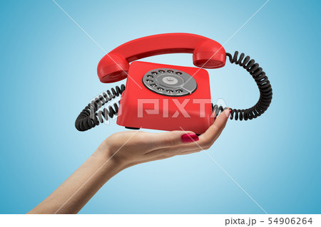 Side closeup of woman's hand facing up and holding ringing retro phone on light blue background. 54906264