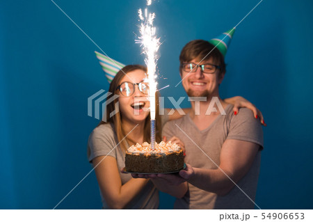 Funny nerd man and woman are wearing holidays caps and glasses holding birthday cake with candles 54906653