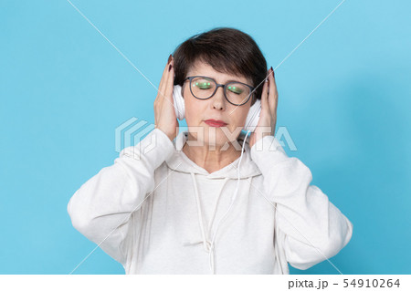 Middle-aged woman listening music on blue background. 54910264