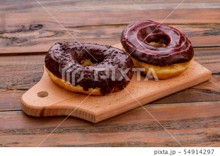 Two chocolate donuts on cutting board. Two chocolate donuts on cutting board. 54914297