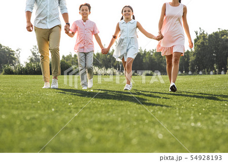 Happy moments. Full length of positive and young family of four holding hands, smiling and walking Happy moments. Full length of positive and young family of four holding hands, smiling and walking 54928193