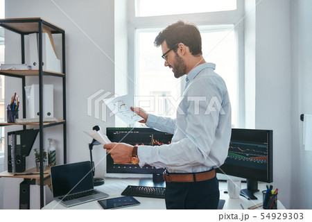 Good news Happy young businessman or trader in eyeglasses and formal wear looking at trading charts Good news Happy young businessman or trader in eyeglasses and formal wear looking at trading charts 54929303