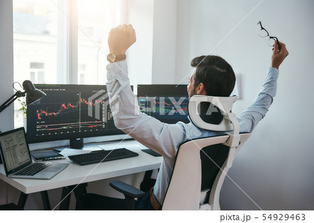 Yes Back view of stock trader with raised hands looking at multiple computer screens with data and 54929463