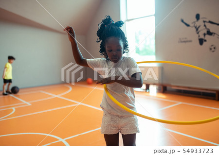 Schoolgirl exercising with hula hoop at sports lesson. 54933723
