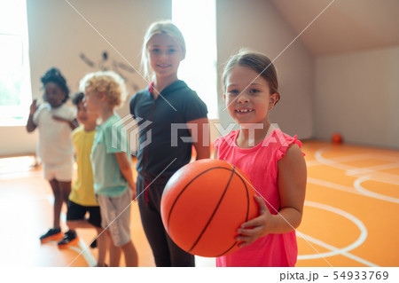 Little schoolgirl with a basketball standing near her classmates. Little schoolgirl with a basketball standing near her classmates. 54933769