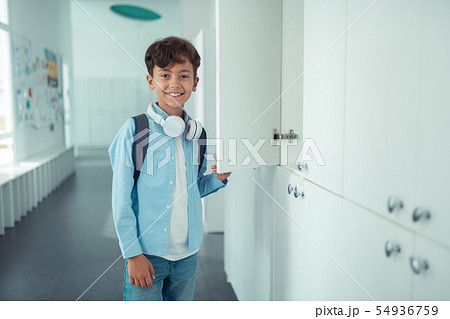 Handsome schoolboy wearing earphones standing near school locker 54936759