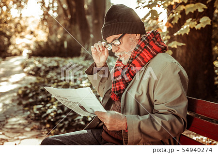 Concentrated aged man attentively reading a newspaper. 54940274