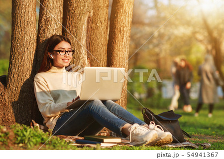 Happy girl sitting with laptop near tree Happy girl sitting with laptop near tree 54941367