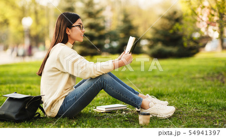 Student girl reading book in park, sitting on grass Student girl reading book in park, sitting on grass 54941397