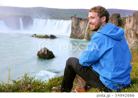 Iceland tourist relaxing by waterfall Godafoss 54942666