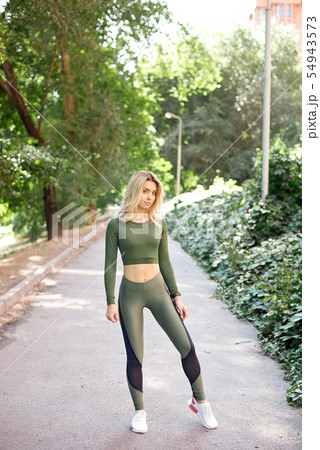 Young slim woman with a sporty body, long blond hair, dressed in a sports top and leggings, prepares 54943573
