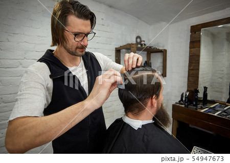 Brutal guy in modern Barber Shop. Hairdresser makes hairstyle a man with a long beard. Master 54947673