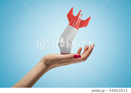 Side closeup of woman's hand facing up and holding small broken rocket upside down, on light blue Side closeup of woman's hand facing up and holding small broken rocket upside down, on light blue 54952615