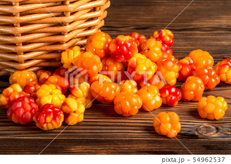 Handful of cloudberry berries poured from a small basket on an old wooden board close-up Handful of cloudberry berries poured from a small basket on an old wooden board close-up 54962537