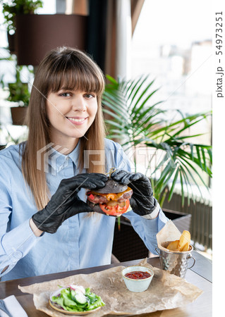 Young woman in blue shirt and black gloves eating delicious juicy hamburger with beef chop. Burgers 54973251
